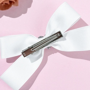 Close-up detail of white satin bow hair clip showing silver metal duckbill clip back