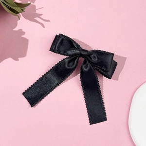Close-up of black satin bow hair clip with wavy edges on a decorative pink background