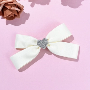 Detailed view of white satin bow hair clip with sparkling rhinestone heart center