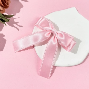 Pink satin bow hair clip with lace trim displayed on a ceramic plate for women