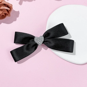 Detail of elegant black satin bow hair clip with a sparkling rhinestone heart decoration