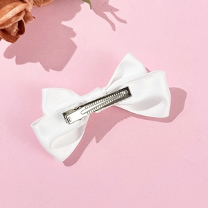 Close-up of a white satin bow hair clip with a silver metal alligator clip detail