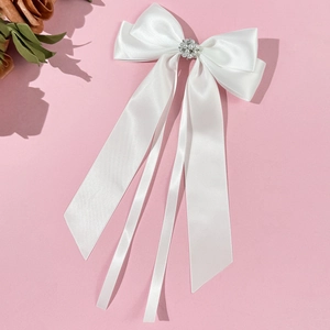 Dettaglio del fiocco in raso bianco con perle e strass su sfondo rosa per acconciature
