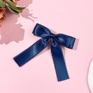 Detailed close-up of dark blue satin bow hair clip with decorative scalloped edges