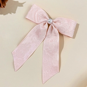 Détail d'une barrette à nœud en jacquard rose avec perle sur tissu dentelle élégant
