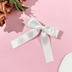 Detailed macro view of a white satin bow hair clip with intricate lace edge on pink surface