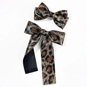 Detail view of two leopard print bow hair clips in shimmering fabric on white background