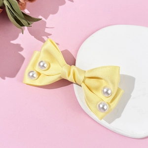 Detailed view of yellow satin bow hair clip with four white pearls on a pink surface