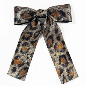 Detailed view of leopard print bow hair clip with metallic thread texture and long ribbons