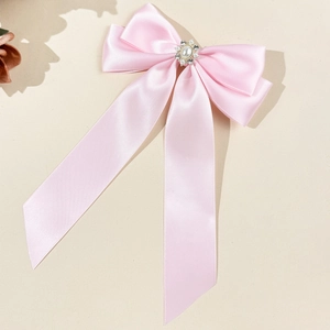 Détail d'une pince à cheveux nœud en satin rose avec perle centrale et strass