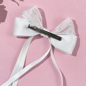 Détail d'une pince à cheveux avec nœud en satin blanc, organza et strass sur fond rose