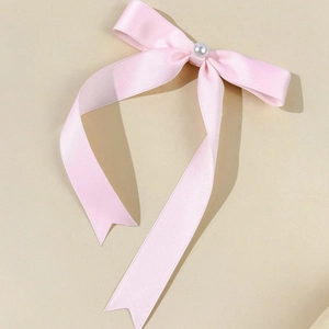 Detailed view of a pink satin bow hair clip with a center pearl and long ribbon tails