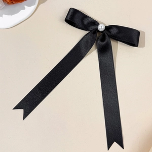 Close-up of black satin bow hair clip with pearl detail and elegant long ribbons
