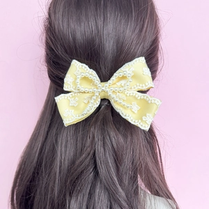 Detalle de horquilla con lazo amarillo con encaje blanco y perlas en el cabello castaño