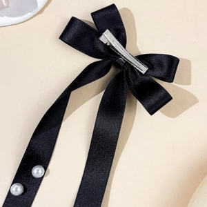 Détail de la pince à cheveux noeud satin noir avec rubans longs et perles élégantes