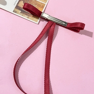 Detail of wine red ribbon bow hair clip showing metal duckbill clip and wavy satin edges