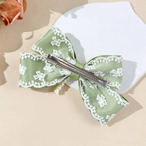 Detalle de lazo de seda verde con encaje floral blanco y colgantes de perlas