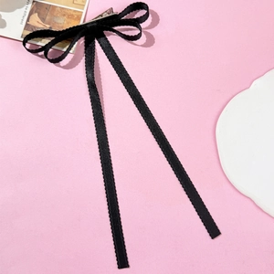Detail of black ribbon bow hair clip with lace edges and long tassels on pink surface