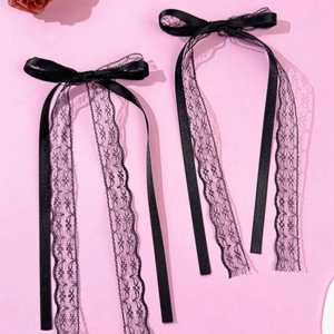 Detail of black satin bow hair clip with translucent wavy lace streamers on pink background