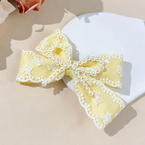 Detalle de una pinza para el pelo con lazo amarillo, encaje blanco y perlas finas