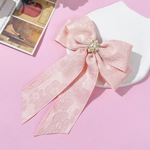 Close-up of pink jacquard bow hair clip with pearl and rhinestone detail on ceramic plate