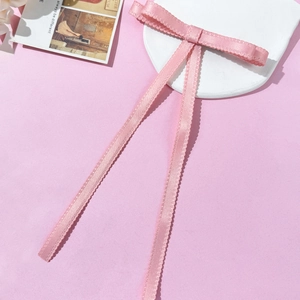 Pale pink satin bow hair clip with long lace edge ribbons on a white stone tray