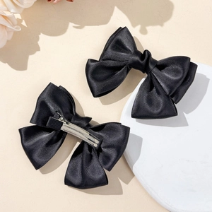 Close-up of black satin bow hair clips showing detailed ribbon texture and metal ducksbill clip