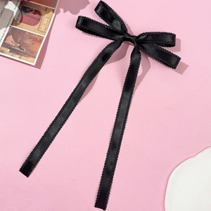 Détail d'un nœud en satin de soie noir avec bords festonnés sur fond rose poudré