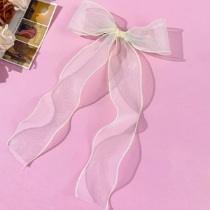 Cream mesh hair bow clip with long streamers and ruffled edges on pink background