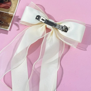 Detail of elegant cream ribbon bow hair clip with sheer tulle streamers on pink background