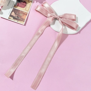 Détail d'une barrette à nœud en soie rose avec bordure en dentelle et longs rubans