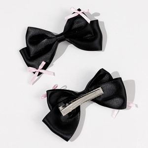 Detail of black satin bow hair clips with pink ribbon accents and metal duckbill clips