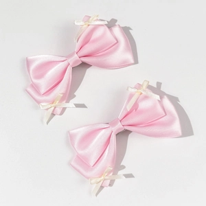 Detailed close-up of two pink satin bow hair clips with white ribbon accents on white background