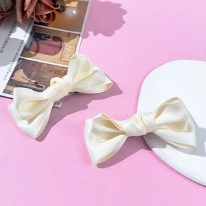 Paar cremefarbene Satin-Schleifen-Haarspangen mit Entenschnabel-Clip auf rosa Grund