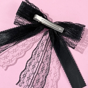 Detail of black lace and satin bow hair clip featuring a silver metal duckbill clip back