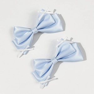 Detailed view of two light blue satin bow hair clips with white ribbon cross accents
