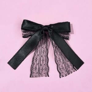 Elegant black satin and lace bow hair clip with wavy scalloped edges on pink background