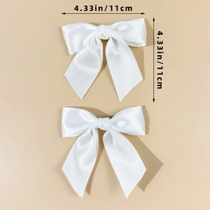 Detail view of white satin bow hair clips showing 4.33 inches dimensions and texture