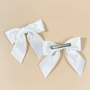Detail shot of two white satin bow hair clips with smooth long ribbons and metal grips