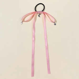 Close-up of pink satin bow hair tie with silver star and moon charms on soft background