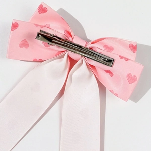 Detailed back view of pink satin bow hair clip with red heart patterns and long ribbons