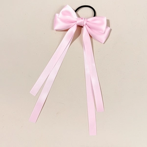 Pink satin bow hair tie with long ribbons and black elastic band on beige background