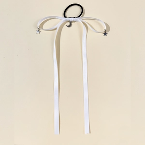 Close-up of white silk ribbon hair tie with silver moon and star charms on cream background