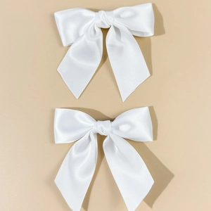 Detail view of two cream white satin bow hair clips on a warm beige background