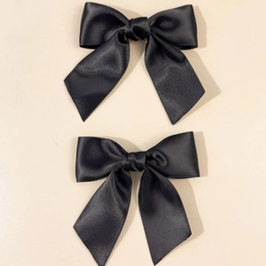 Detail view of two black satin bow hair clips with a silky finish on beige background