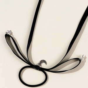 Elegant black ribbon hair tie with silver moon and star charms on cream background