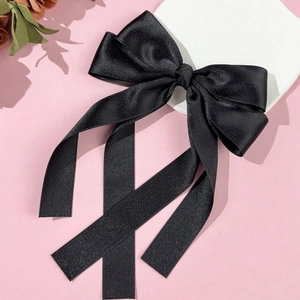Elegant black satin bow hair clip with long ribbons on pink decorative background