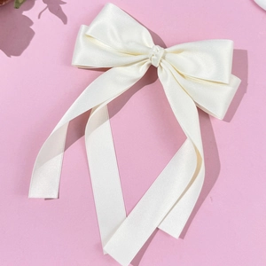Close-up of cream white satin bow hair clip with long ribbons on pink background