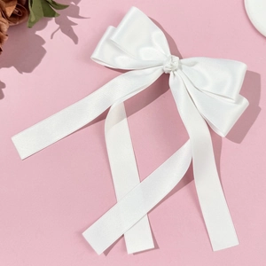 Close-up of white satin bow hair clip with long ribbons on pink background