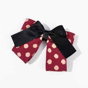 Détail d'une pince à cheveux avec nœud à pois bordeaux et ruban de satin noir